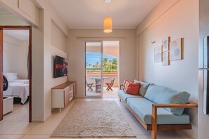 Ein modernes Wohnzimmer mit einer Couch, einem Fernseher und einer Glastür, die auf einen Balkon führt.