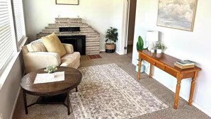 Una sala de estar acogedora con chimenea, un sofá, una mesa de centro y un cuadro en la pared.