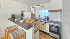 Een kleine keuken met een fornuis, koffiezetapparaat en een fruitschaal op het aanrecht.