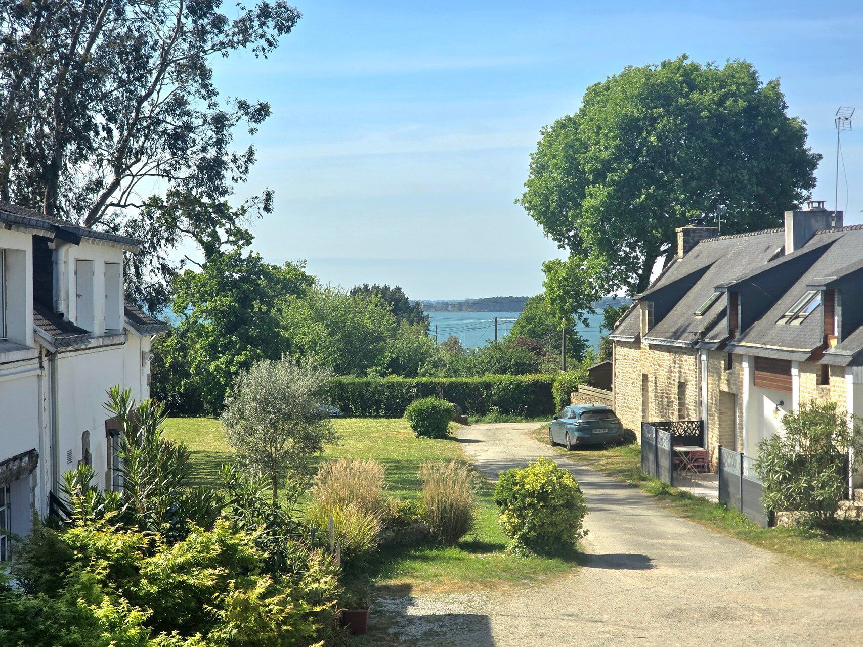 A residential street with houses, a gravel path, and a view of the sea.