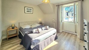 Een slaapkamer met een bed, nachtkastjes, een hanglamp, een raam met gordijnen en een radiator.