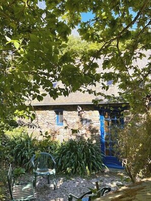 A stone building with a blue door, surrounded by greenery and a garden with a chair. - La Bergerie, a cozy duo between land and sea (Plouha)
