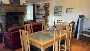 Un salon chaleureux avec une cheminée, une table à manger avec des chaises, un canapé rouge et un escalier.
