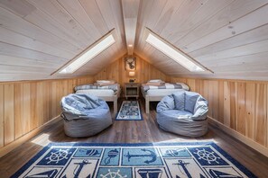 Une chambre mansardée chaleureuse, avec deux lits, une lucarne et un tapis sur le thème de la marine.