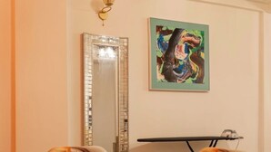 Ein Essbereich mit einem Glastisch, Stühlen mit Kissen, einer dekorativen Schale, einem Spiegel und einem Gemälde an der Wand.