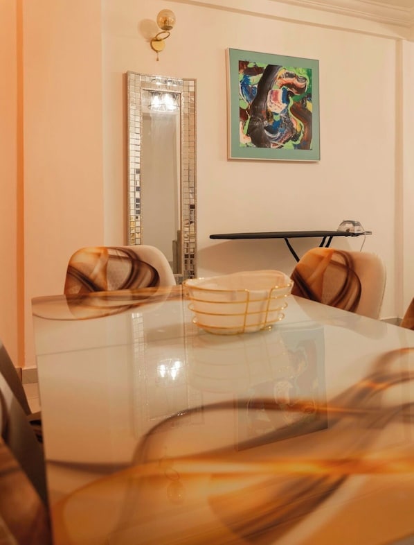 Un comedor con una mesa de vidrio, sillas con cojines, un cuenco decorativo, un espejo y un cuadro en la pared.