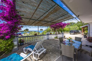 A covered outdoor seating area with lounge chairs and a table, overlooking a scenic view. - Sea View Apartment Ankica with Terrace (Kampor)