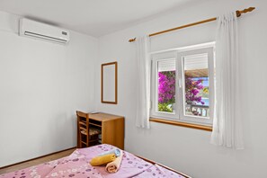 A room with a bed, a desk, a chair, a window with curtains, and an air conditioning unit. - Sea View Apartment Ankica with Terrace (Kampor)