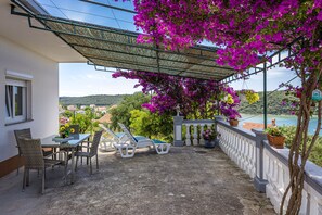 A balcony with a table, chairs, and sun loungers, overlooking a scenic landscape with hills and a body of water. - Sea View Apartment Ankica with Terrace (Kampor)
