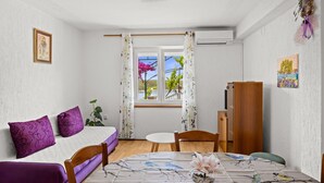 Ein Zimmer mit einem Bett, einem Esstisch, einem Stuhl, einem kleinen Tisch und einem Fenster mit Vorhängen.