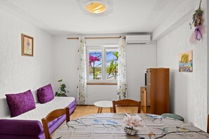 Quarto com cama, mesa de jantar, cadeira, mesinha e janela com cortinas.