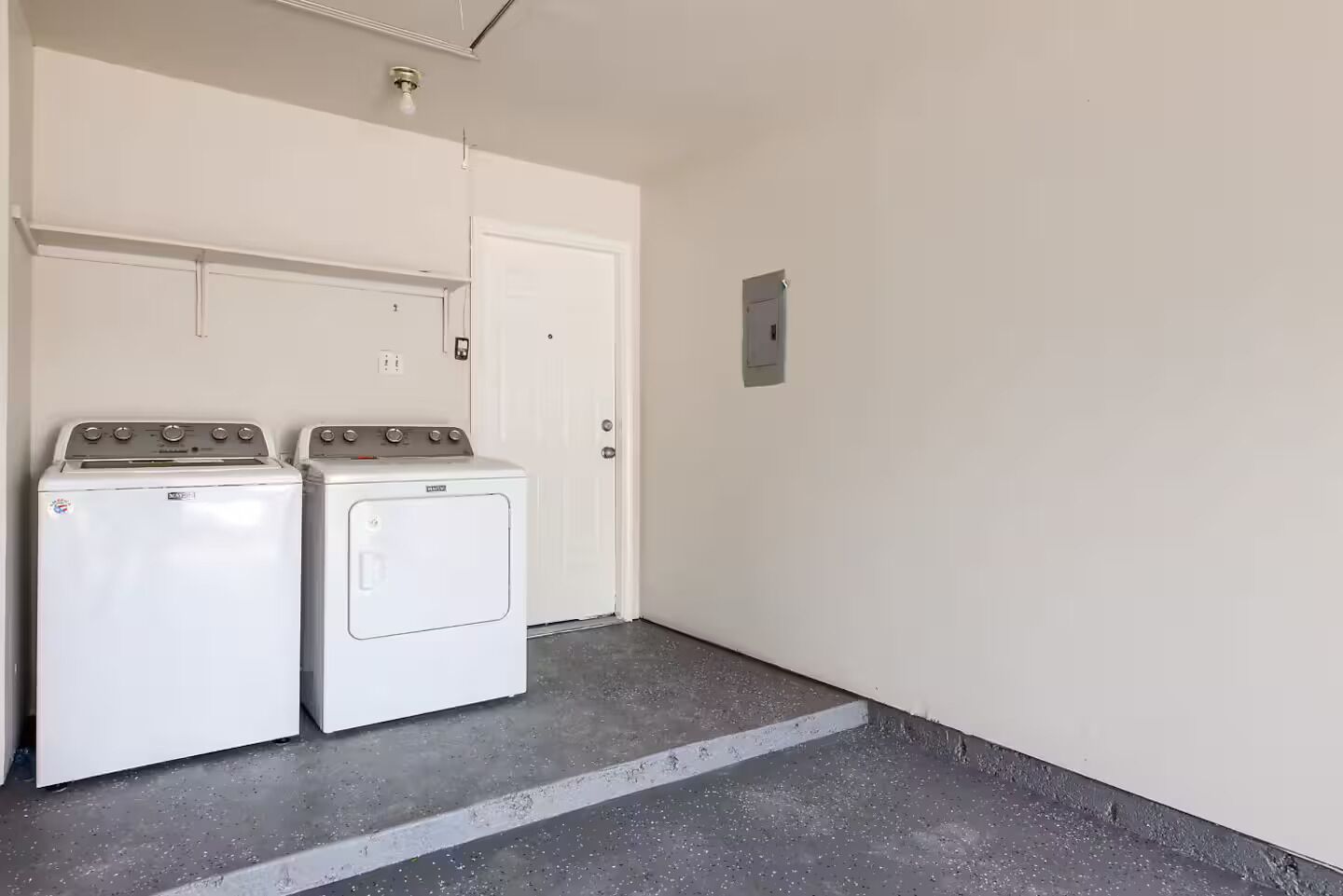 A laundry room with two white front-loading washers and dryers, a white door, and a small electrical outlet on the wall.