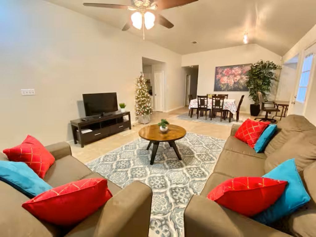 A living room with a sofa set, a coffee table, a TV, a Christmas tree, and a dining area.