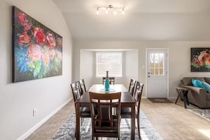 A dining area with a table and chairs, a painting on the wall, a window with blinds, and a door. - Modern 3/2 Private Home NW Austin (Austin)
