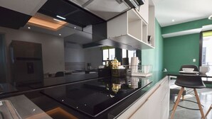 Cuina moderna amb una illa central, electrodomèstics integrats i zona de menjador amb una cadira i taula.