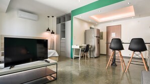 Un apartament modern amb zona de estar que inclou una televisió de pantalla plana, taula de dinar amb cadires, petita cuina i un espai de treball.
