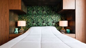 Un lit avec un matelas blanc, flanqué de deux tables de chevet en bois, sur lesquelles sont posées des lampes et des objets décoratifs.