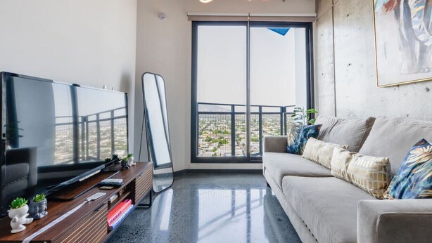 Un salon moderne doté d’un téléviseur à écran plat, d’un canapé et d’une grande fenêtre donnant sur un balcon.