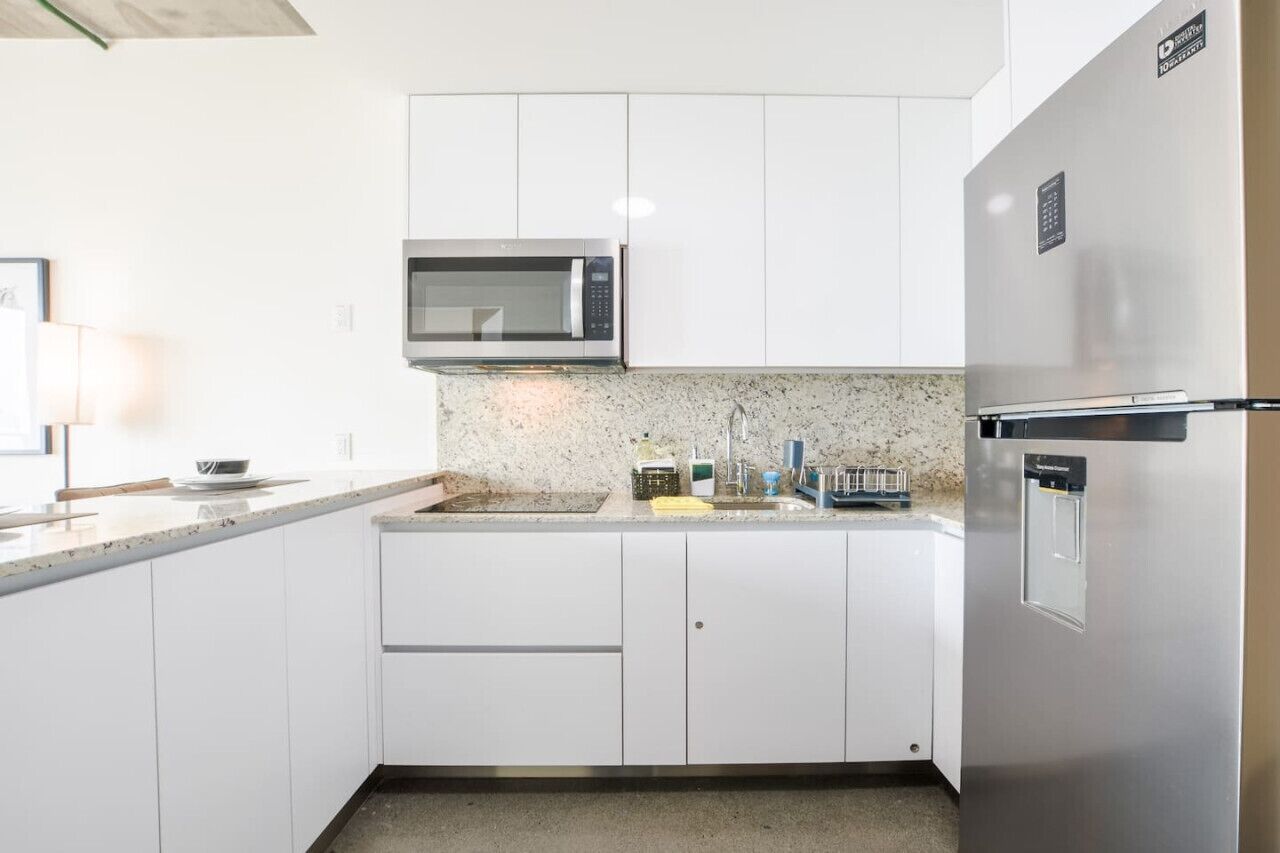 A modern kitchen with white cabinets, a stainless steel microwave, and a built-in refrigerator.