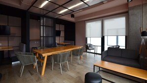 A modern office space with a wooden conference table, grey chairs, a black sofa, and large windows.