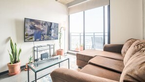 A modern living room with a large flat-screen TV, a sofa, and potted plants.