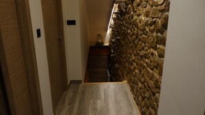 Een smalle gang met houten vloeren, een stenen muur aan de ene kant, en een houten deur aan de andere kant.