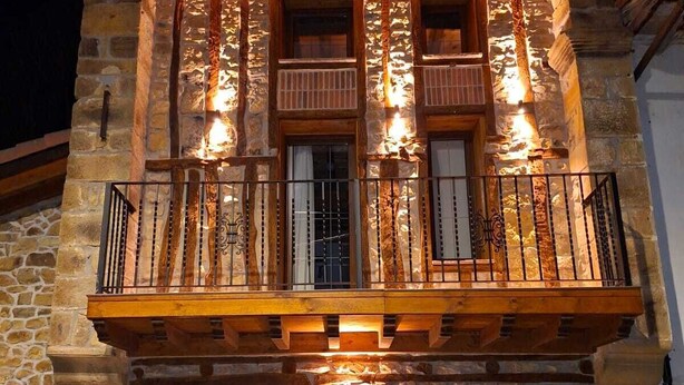 Een stenen gebouw met een houten balkon, een bankje en een groot rad.