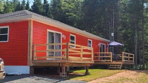 A red cabin with a wooden deck and a covered outdoor seating area.