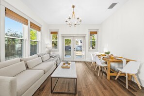 A spacious living room with a sofa, coffee table, and dining area with chairs and a table. - Design-Forward New Build · 3BR/2BA · Seminole Heights (Tampa)