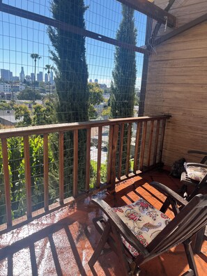 A wooden balcony with a metal railing, a chair with a patterned cushion, and a view of a cityscape through a wire mesh. - Gorgeous dream house 1 plus in Silver Lake Los Angeles, Stunning views! Peaceful (Los Angeles)