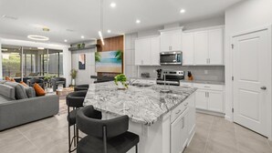 Una cocina moderna con armarios blancos, una isla de mármol y electrodomésticos de acero inoxidable.