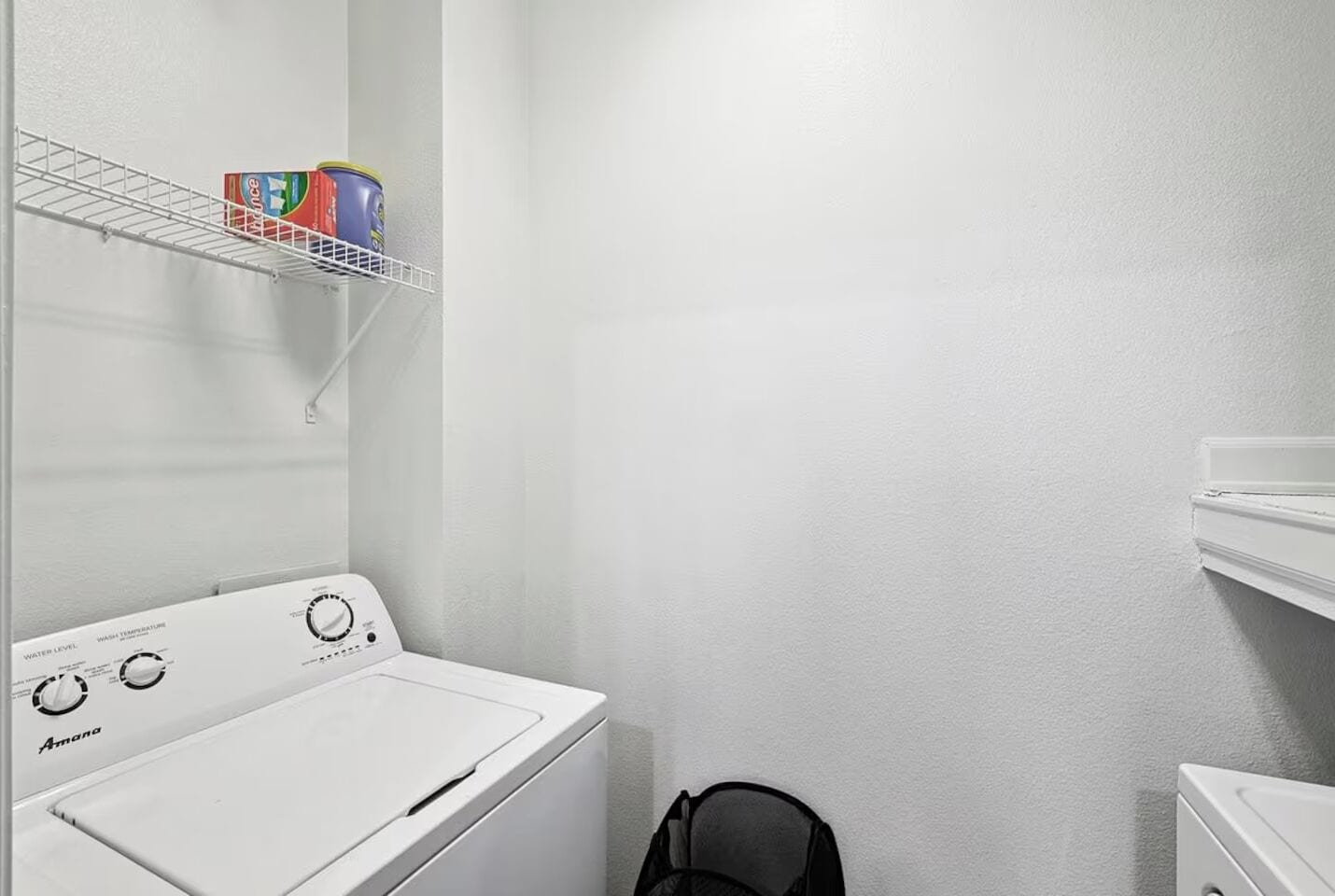 Un espace buanderie comprenant un lave-linge blanc, une étagère avec de la lessive et un sèche-linge.