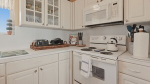 A kitchen with white cabinets, a microwave, a stove, and various kitchen utensils. - Casa Bonita Surfside (Freeport)
