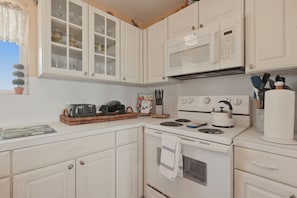 A kitchen with white cabinets, a microwave, a stove, and various kitchen utensils. - Casa Bonita Surfside (Freeport)