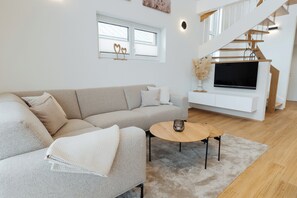A modern living room with a beige sectional sofa, a round coffee table, and a flat-screen TV mounted on a white wall.