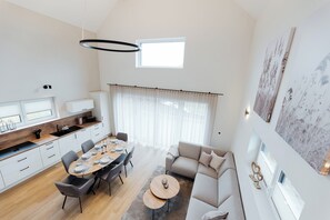 A modern kitchen with a dining area, a sofa, and a large window with curtains.