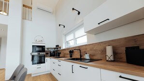 Eine moderne Küche mit weißen Schränken, einer Holzausziehtafel, einem eingebauten Backofen und einem schwarzen Kühlschrank.