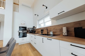 A modern kitchen with white cabinets, a wooden countertop, a built-in oven, and a black refrigerator. - Newly built vacation home near the Geierlay suspension rope bridge (Mörsdorf)
