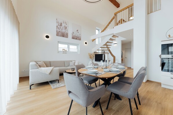 A spacious living area with a dining table set for six, a sofa, and a staircase leading to an upper level.