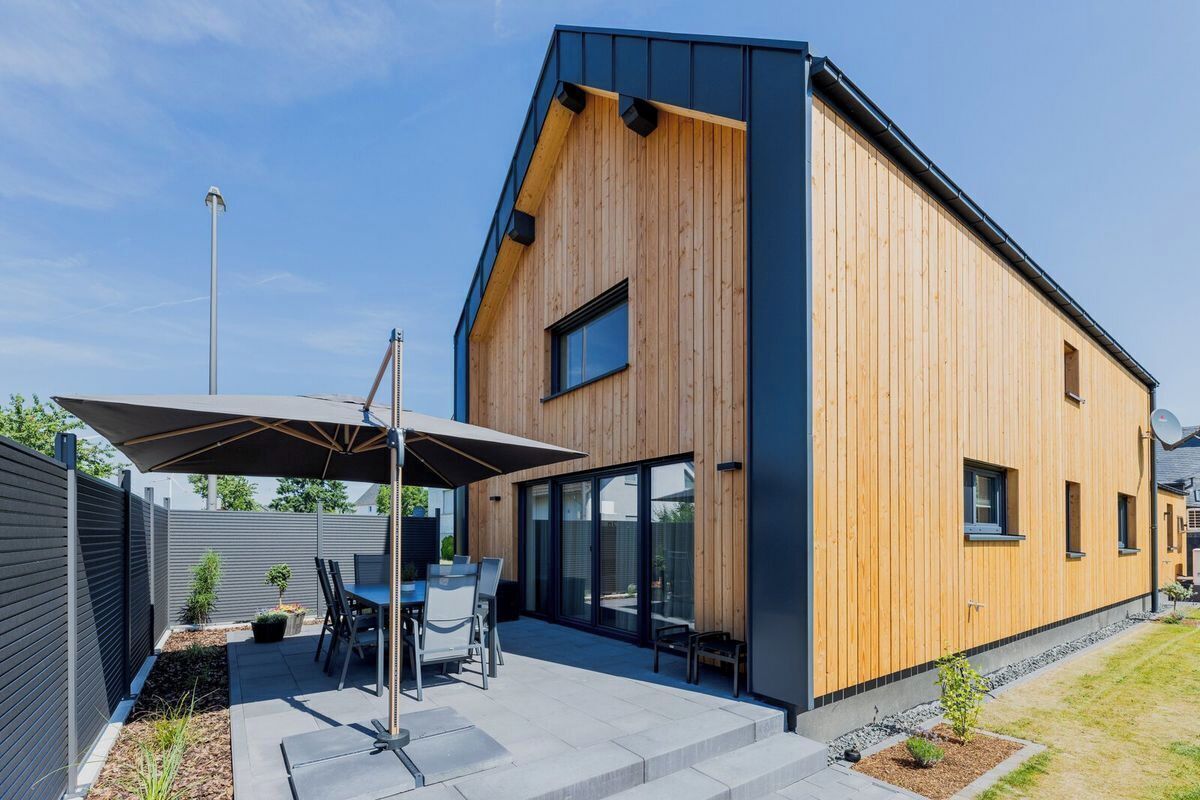 Ein modernes Haus mit Holzfassade, einer Terrasse und Gartenmöbeln sowie einem großen Fenster.
