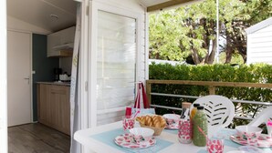 An outdoor dining area with a table set for two, featuring floral tableware and a basket of croissants. - Palmyre - Confort 1 - 3p (1) (Les Mathes)
