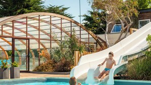 Ein Poolbereich mit Rutsche, einem Gewächshaus und einer Person im Wasser.