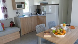 Eine kleine Küche mit Mikrowelle, Herd und Kühlschrank. Ein Esstisch mit Stühlen und einer Obstschale steht in der Mitte.
