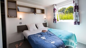 Un dormitorio con cama, mesitas de noche, una ventana con cortinas y estanterías empotradas.