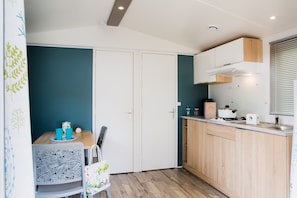 Een compacte keuken met houten kastjes, een wit aanrechtblad en een wand in blauwgroen.