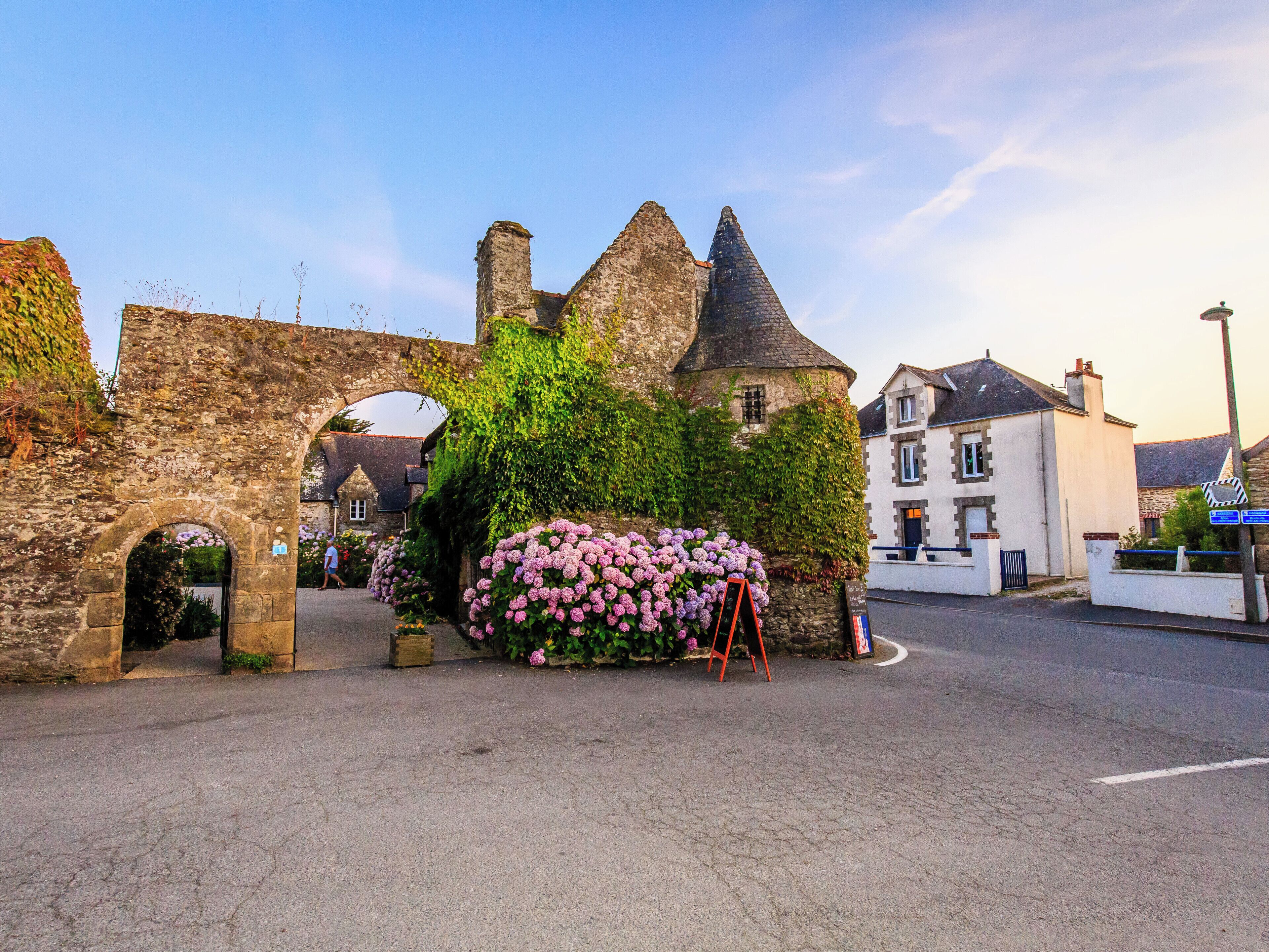 A stone archway leading to a building with ivy-covered walls and a large flower display.