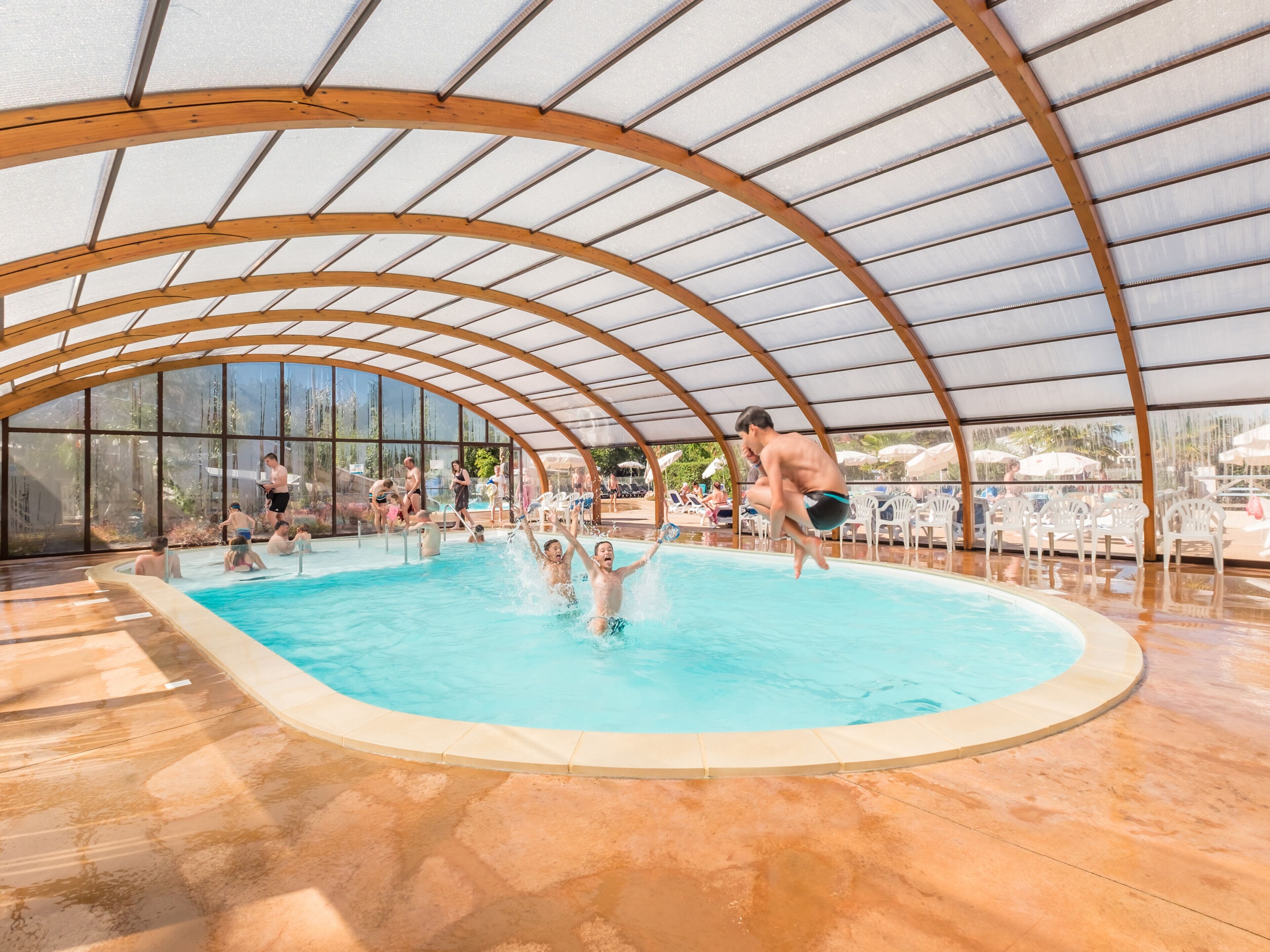 An indoor swimming pool with a curved wooden roof and clear glass walls.