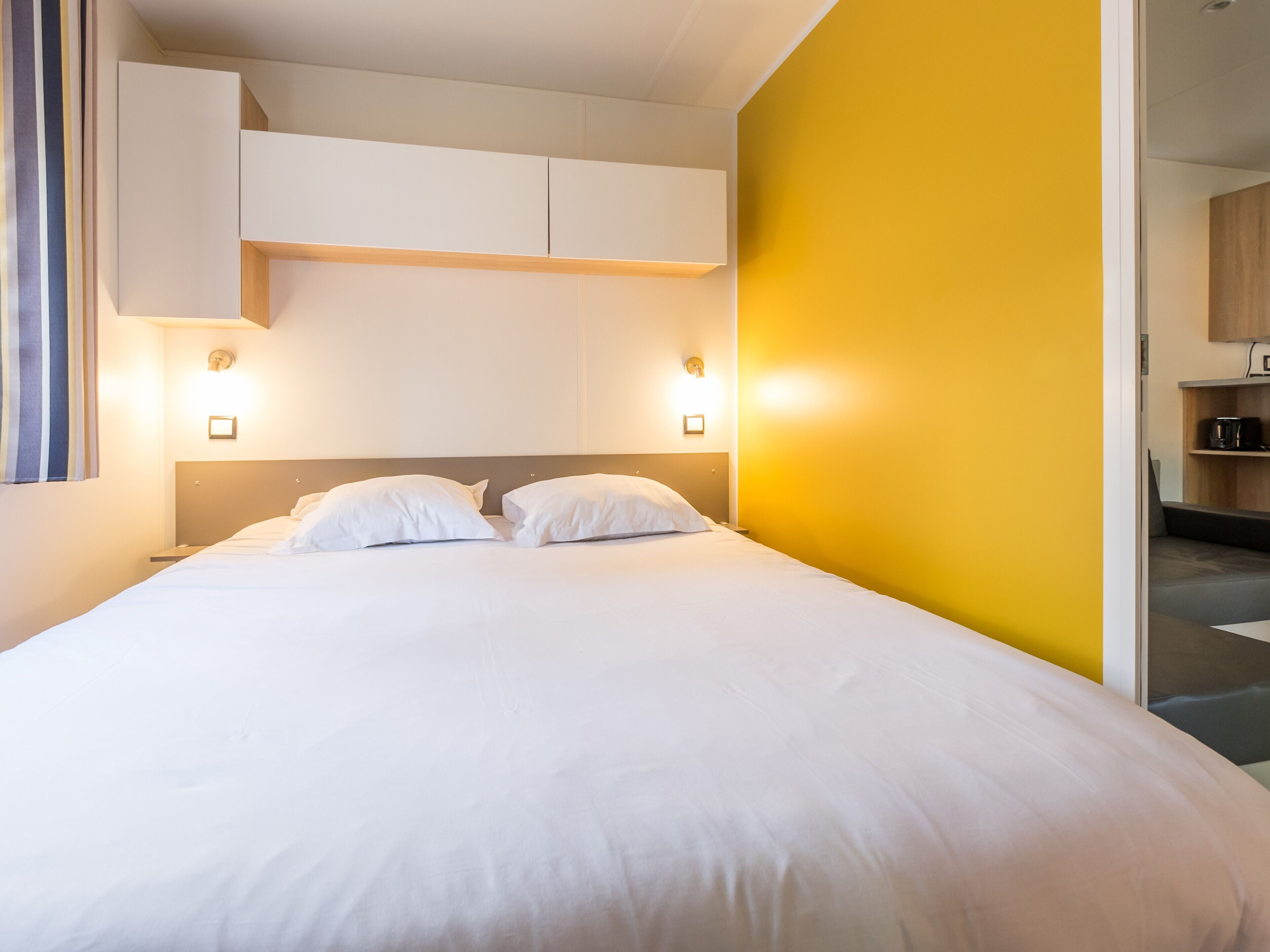 Een moderne hotelkamer met een groot bed, wit beddengoed en een felgele accentmuur.