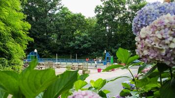 Un parque con mesas de picnic, una estructura de juego azul y abundante vegetación.
