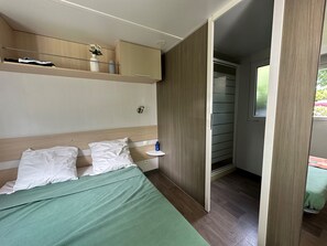 A bedroom with a bed, pillows, a bedside table, a shelf with items, and a wardrobe.
